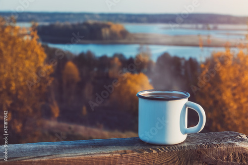 Enameled cup of coffee or tea on autumn landscape outdoors.