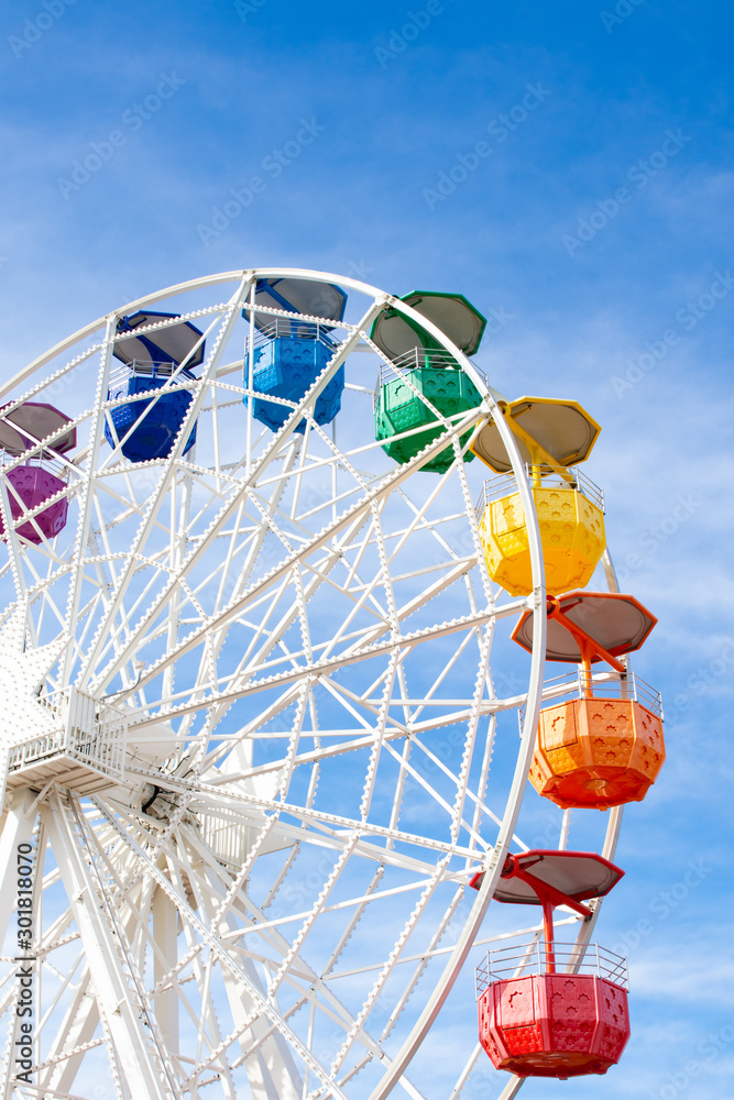 Ferris wheel with white structure and colored cabins on background of blue sky Ferris wheel with white structure and colored cabins on background of blue sky