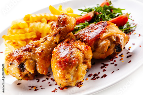 Roast chicken drumsticks with french fries and vegetables on white background