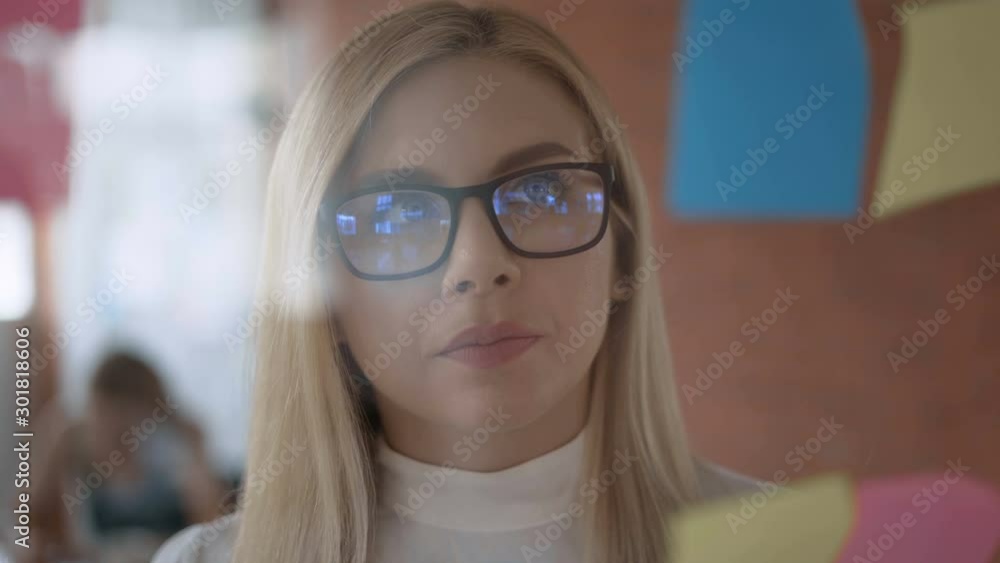 modern successful blond woman working in an office on a project. woman stands in front of a transparent board with notes 4K modern successful blond woman working in an office on a project. woman stands in front of a transparent board with notes 4K