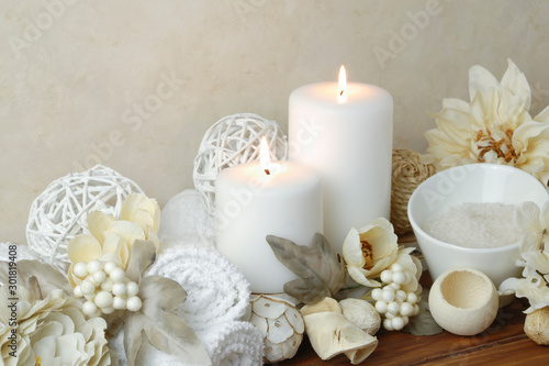 spa concept of white burning candles arranged with natural potpourri elements and flowers with bath slats on a warm background