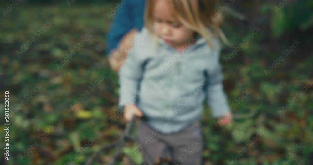 Little toddler waving sticks around with his mother in the background Little toddler waving sticks around with his mother in the background