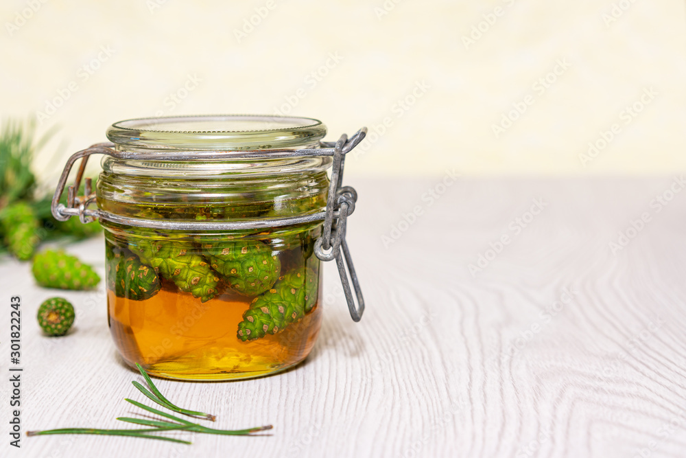 Closed glass jar of honey with young green pine cones on a light wooden table. Gourmet Dessert. Natural medicine Closed glass jar of honey with young green pine cones on a light wooden table. Gourmet Dessert. Natural medicine