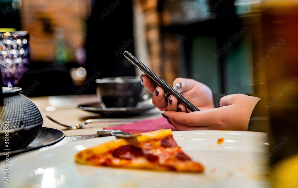 Fototapeta premium woman hand using mobile phone in cafe with a piece of pizza in plate on table
