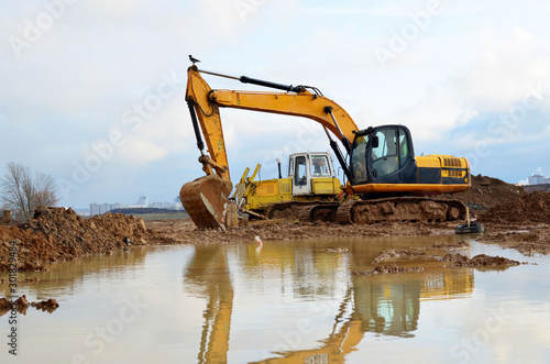 Tracked excavator working at a construction site during laying or replacement of underground storm sewer pipes. Installation of water main, sanitary sewer, storm drain systems - Image