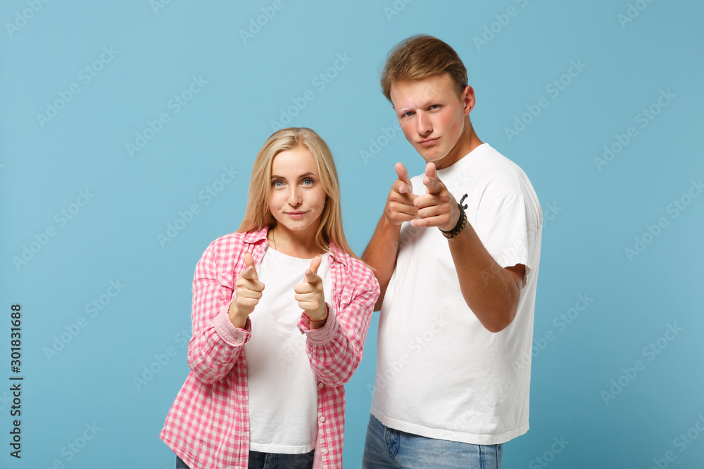 Young couple two friends guy girl in white pink empty blank design t-shirts posing isolated on pastel blue background. People lifestyle concept. Mock up copy space. Pointing index fingers on camera. Young couple two friends guy girl in white pink empty blank design t-shirts posing isolated on pastel blue background. People lifestyle concept. Mock up copy space. Pointing index fingers on camera.