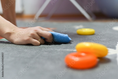 Mother woman is wiping the carpet in the children room with a damp cloth close up.