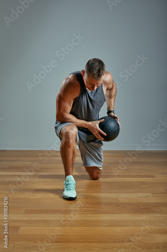 Strong man doing exercise with med ball. Photo of man perfect physique on grey background. Strength and motivation.
