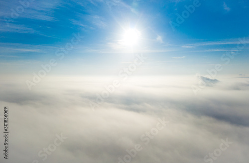 Fototapeta Naklejka Na Ścianę i Meble -  Aerial photo above the fog or white clouds with shining sun. Beautiful sunrise cloudy sky from aerial view. Above clouds from airplane window or drone.