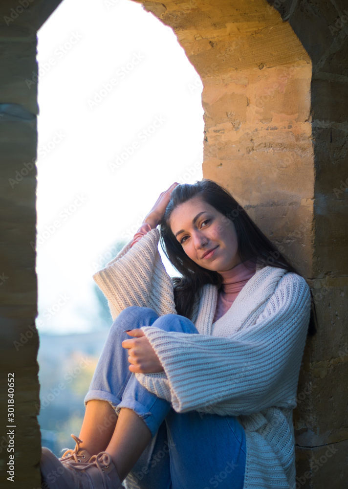 young girl in a white cardigan sitting in the antique arch window opening