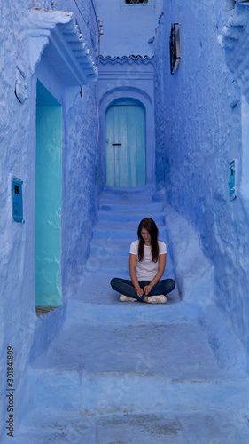 Girl sits on the stairs in a narrow blue street of the old Medina in Chefchaouen town in Morocco.  © vadim_ozz