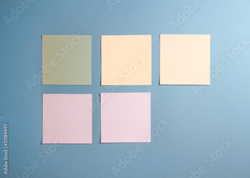 5 blank empty white and pastel colors sticky notes on clean blue background with free space, from top view with copy space