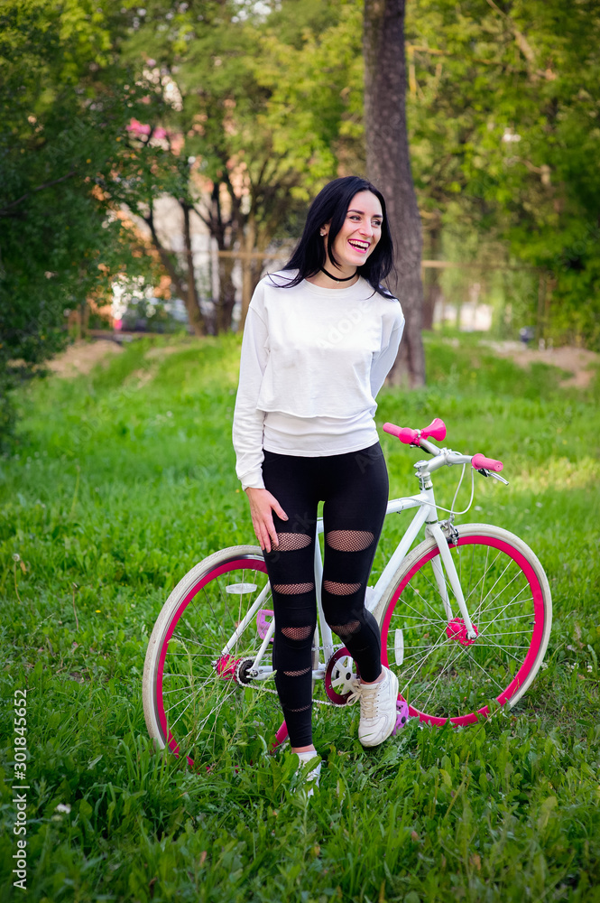 Naklejka premium girl on a red and white bike. A pretty young sexy tanned athletic girl rides in nature. cheerful and smiling brunette. good figures.