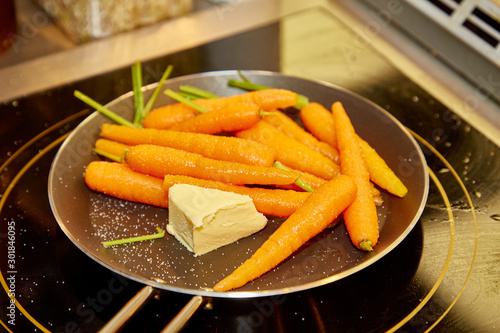 Whole young carrots are fried with butter in a skillet.