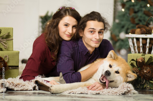 Young happy couple cuddling adorable akita inu dog with on the floor for Christmas holidays at home. © Kate