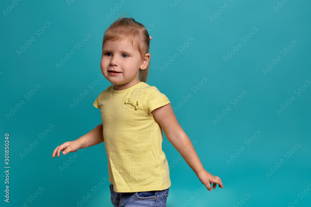Close-up studio shot of a beautiful little girl. Little blonde girl in a yellow T-shirt on a blue background. The emotions of a child. Close-up studio shot of a beautiful little girl. Little blonde girl in a yellow T-shirt on a blue background. The emotions of a child.