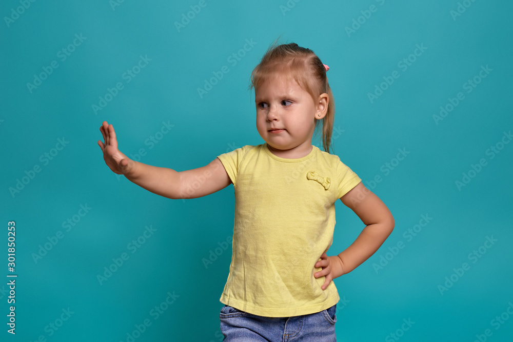 Close-up studio shot of a beautiful little girl. Little blonde girl in a yellow T-shirt on a blue background. The emotions of a child. Close-up studio shot of a beautiful little girl. Little blonde girl in a yellow T-shirt on a blue background. The emotions of a child.