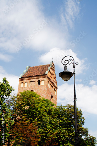 An old brick tower and a lantern against a background of green thickets and blue sky. The urban landscape in Warsaw, Poland.