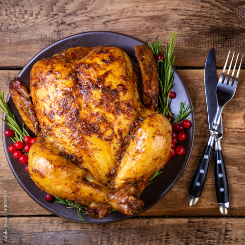 Cooked chicken for festive dinner. Cooked whole chicken or turkey with herb rosemary and berries on wooden table. Christmas, Thanksgiving day, holidays concept