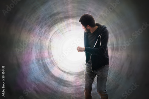 Young man is running away from bright light rays inside tunnel.