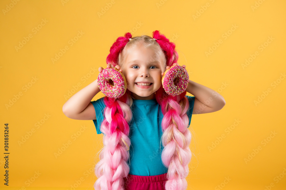 little girl with donuts on yellow background isolate, space for text