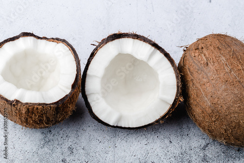 The ripe coconut is split in half, whole coconut, on light gray background, close up, top view