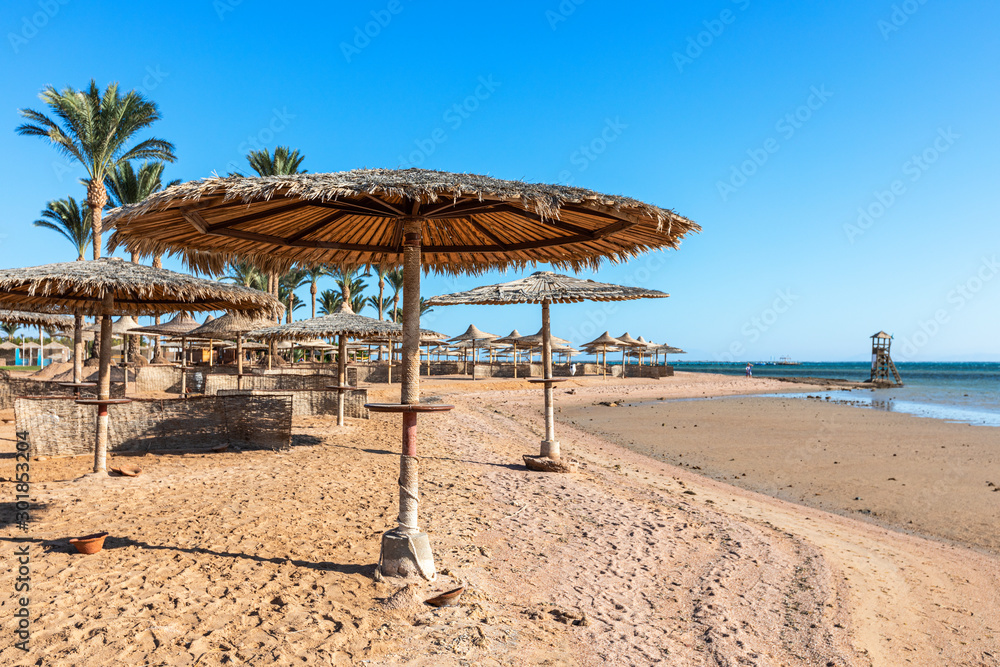 Beach with straw umbrellas and sunbeds. Egyptian resort in Sharm el Sheikh. Vacation concept.