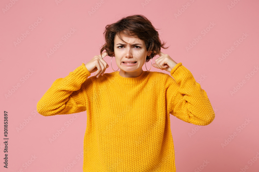 Displeased confused young brunette woman girl in yellow sweater posing isolated on pastel pink background, studio portrait. People lifestyle concept. Mock up copy space. Covering ears with fingers. Displeased confused young brunette woman girl in yellow sweater posing isolated on pastel pink background, studio portrait. People lifestyle concept. Mock up copy space. Covering ears with fingers.