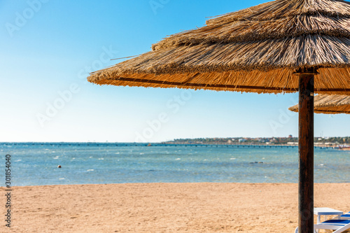 Fototapeta Naklejka Na Ścianę i Meble -  Beach with straw umbrellas and sunbeds. Egyptian resort in Sharm el Sheikh. Vacation concept.
