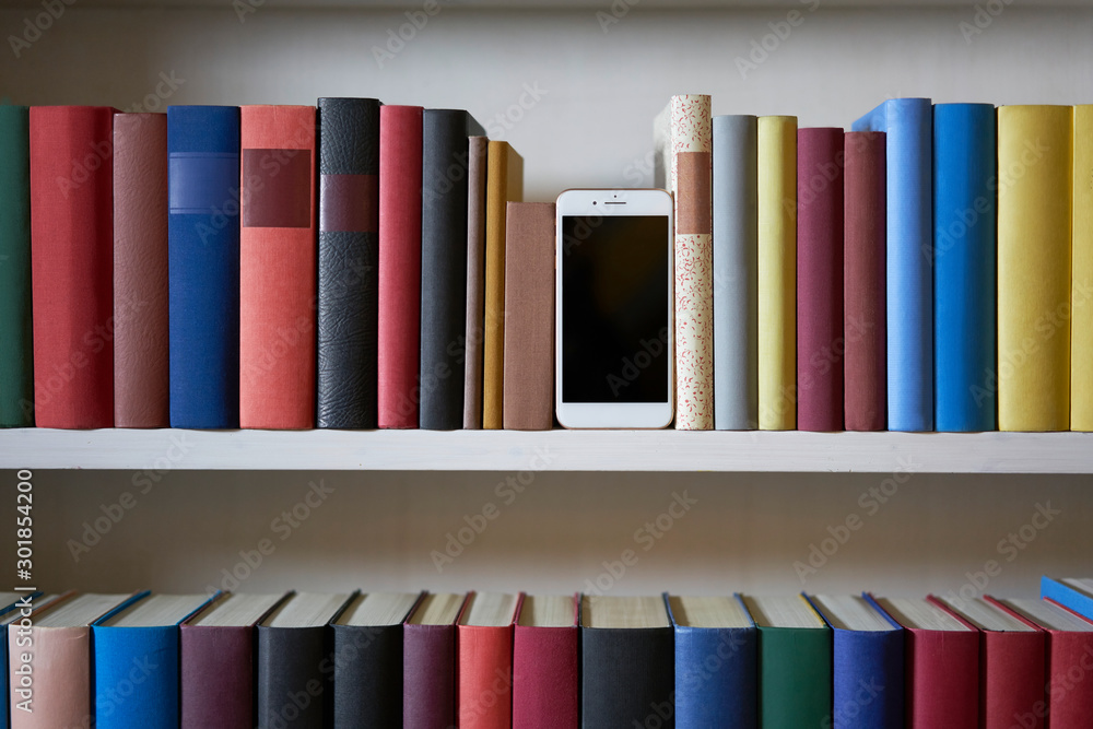 Fototapeta premium Mobile phone in bookshelf with sorted books