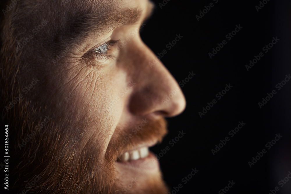 Side view closeup of handsome adult man smiling happil y while watching TV at night, profile outlined against dark background, copy space Side view closeup of handsome adult man smiling happil y while watching TV at night, profile outlined against dark background, copy space