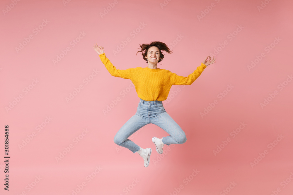Smiling young brunette woman girl in yellow sweater posing isolated on pastel pink background. People lifestyle concept. Mock up copy space. Jumping, hold hands in yoga gesture, relaxing meditating.