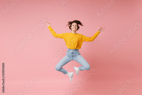 Smiling young brunette woman girl in yellow sweater posing isolated on pastel pink background. People lifestyle concept. Mock up copy space. Jumping, hold hands in yoga gesture, relaxing meditating.