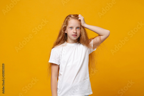 Shocked perplexed little ginger kid girl 12-13 years old in white t-shirt isolated on yellow background children studio portrait. Childhood lifestyle concept. Mock up copy space. Putting hand on head.