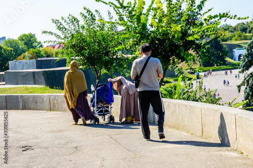 Muslim man with his wives and baby carriage walking in a city park