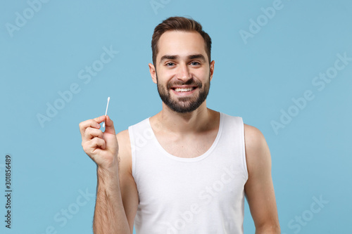 Bearded man 20s years old in white shirt hold cotton swab stick for ear cleaning isolated on blue pastel background studio portrait. Skin care healthcare cosmetic procedures concept Mock up copy space