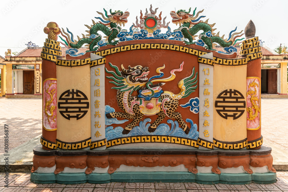 Obraz premium Nha Trang, Vietnam - March 11, 2019: Dinh Phu Vinh community center and celebration hall. Decorative beige and maroon short wall with Dragon fresco and statues under silver sky.