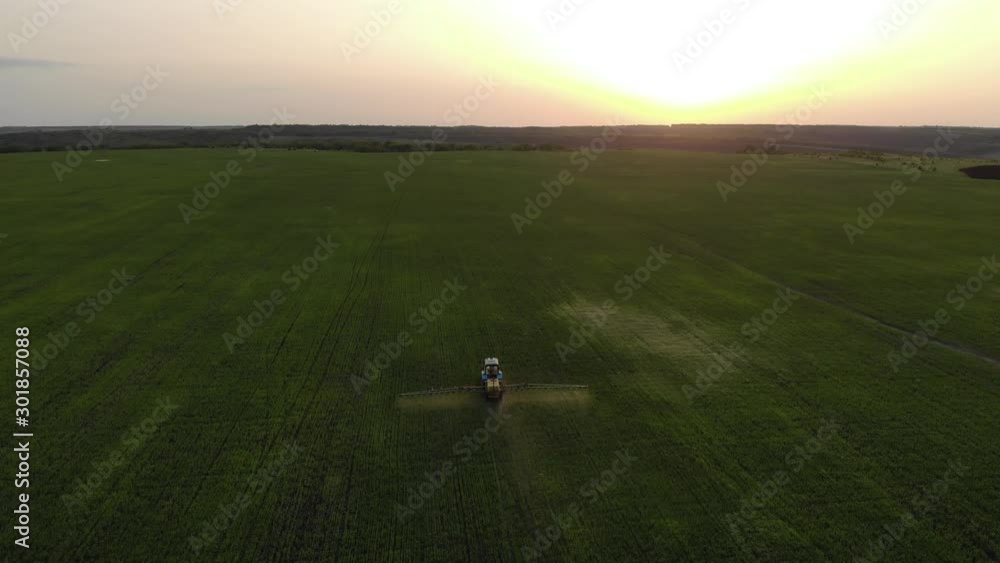 Aerial view of farming tractor spraying on field with sprayer, herbicides and pesticides at sunset. Farm machinery spraying insecticide to the green field, agricultural natural seasonal spring works. Aerial view of farming tractor spraying on field with sprayer, herbicides and pesticides at sunset. Farm machinery spraying insecticide to the green field, agricultural natural seasonal spring works.