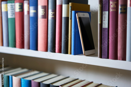 Mobile phone standing upright between books in bookcase
