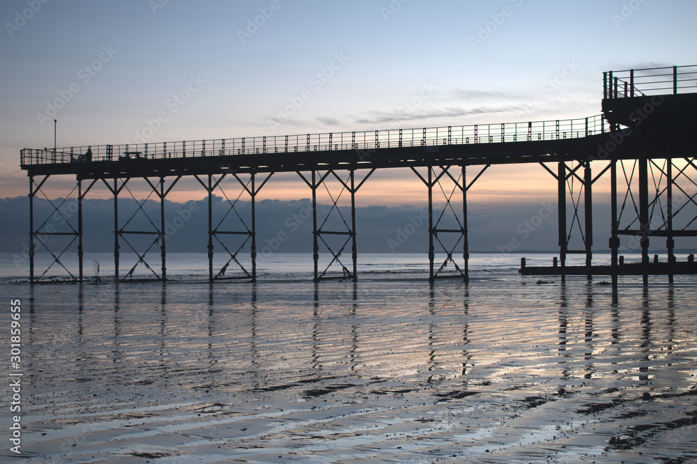 Bognor Regis historic Pier with a beautiful sunset behind and reflections on the sand at low tide.