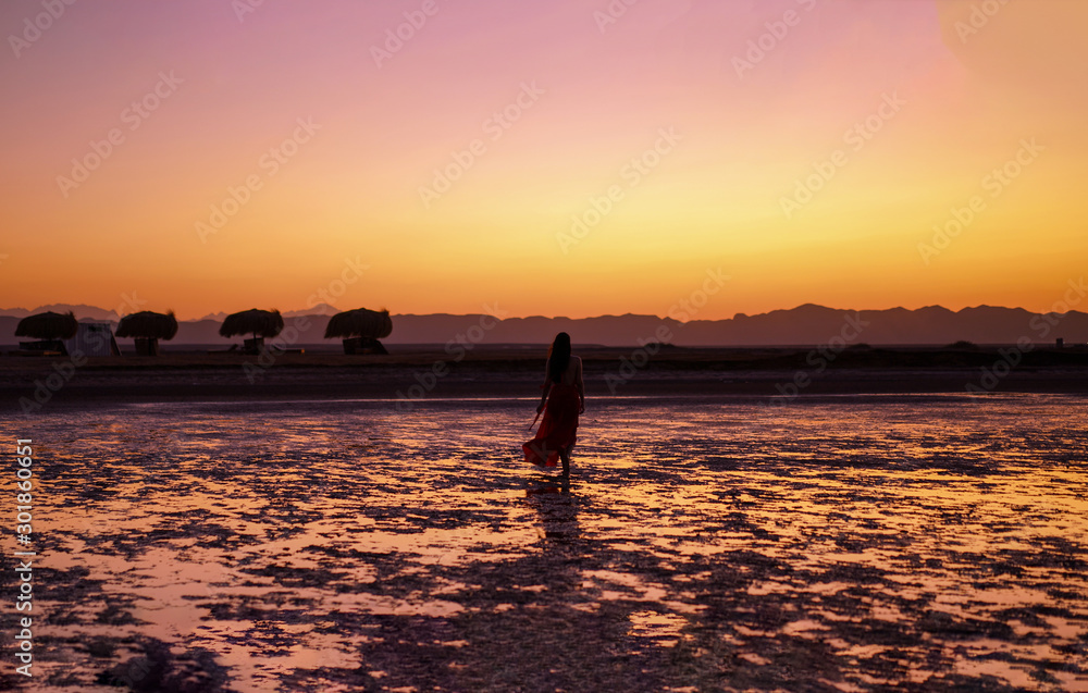 Beautiful women walking on the beach during a fire sunset with stunning view of the Red Sea mountains in the background 