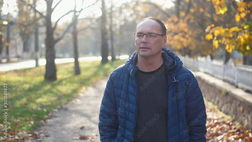 middle aged handsome relaxed man in glasses walking in the autumn park in slow motion middle aged handsome relaxed man in glasses walking in the autumn park in slow motion