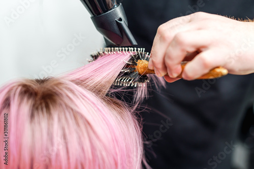Hands of hairdresser are drying short pink hair with a hairdryer close up.