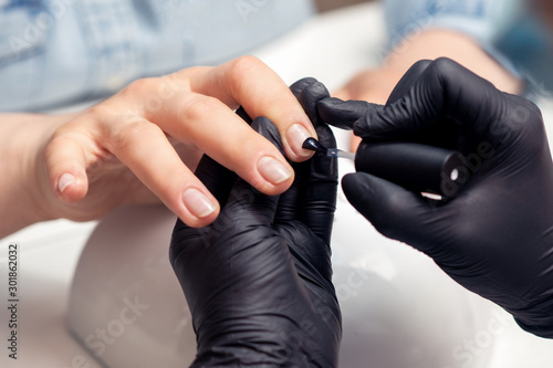 Female beautician is applying nail polish to female nail in a beauty salon close up.
