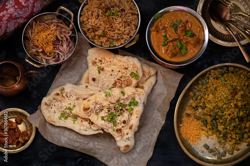 Indian naan, korma, pilaf and side dishes on dark background