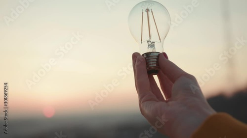 Young hands woman holds a house light bulb at sunset renewable energy nature electricity innovation green invention responsibility environment adult power protect lamp slow motion