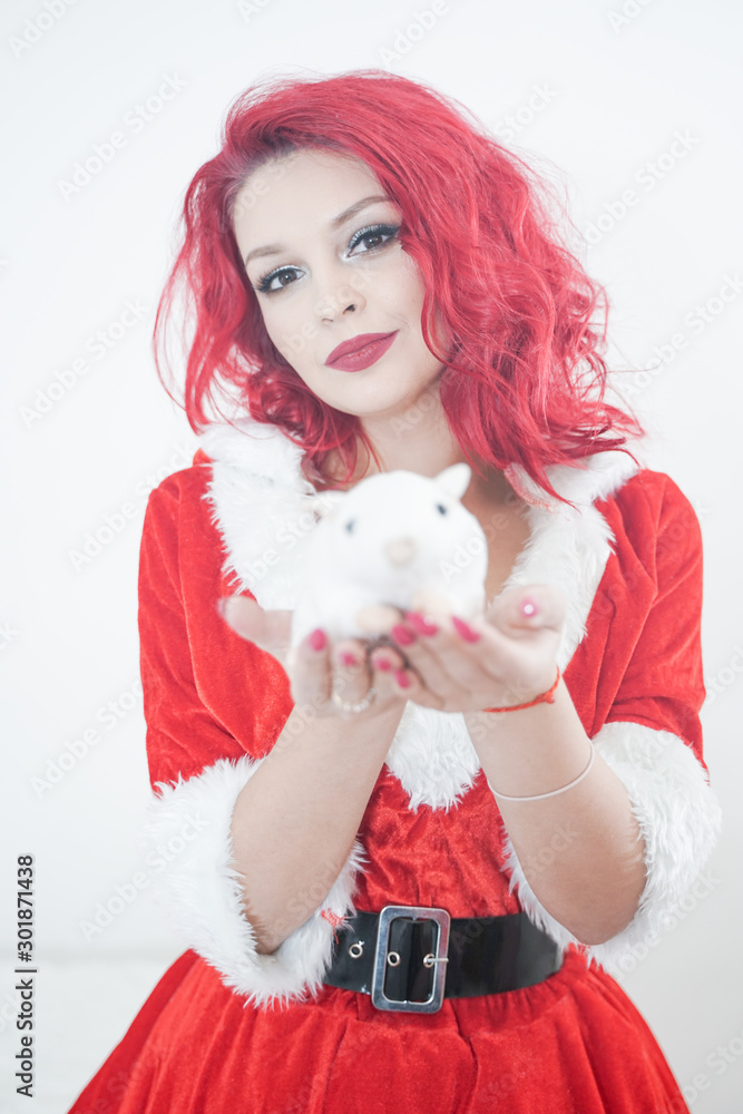 pretty redhaired young stylish woman in velvet santa dress with fur posing on white room background near the cozy window with symbol of 2020 year plush toy of white rat mouse pretty redhaired young stylish woman in velvet santa dress with fur posing on white room background near the cozy window with symbol of 2020 year plush toy of white rat mouse