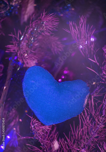 Christmas background-purple heart of canvas on a background of fir branches with lilac backlight, futuristic neon holiday background, vertical frame photo