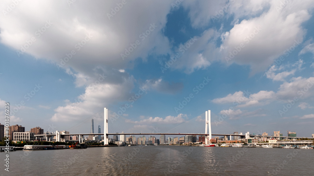 Shanghai Nanpu bridge viewed in middle of Huangpu river with white clouds and blue sky background, the four Chinese characters on bridge means Nanpu bridge.