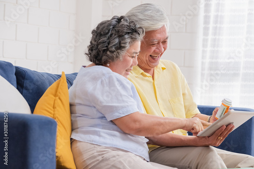 Asian senior couple use tablet video conference with doctor about pill  while sitting on sofa at home,senior learn to use technology.aging at home photo